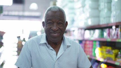 One happy African American senior man pushing shopping cart at grocery store. Portrait of an elderly black consumer at local business store aisle with products