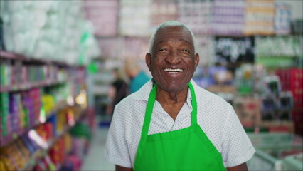 One happy black older employee of local store smiling at camera. African American senior manager of grocery store wearing apron with joyful emotion, employee job occupation concept