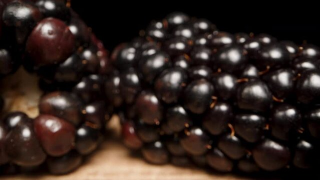 The large blackberry is scattered on a wooden table against a black background. Dolly slider extreme close-up.