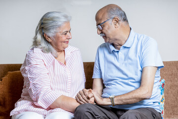 Indian couple sitting on sofa with head joint together having Quality time together , after Retirement life 