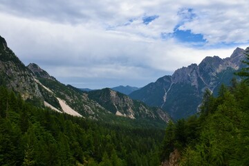 Fototapeta na wymiar Forest covered valley bellow Vrsic pass and mountains in the Julian alps in Gorenjska, Slovenia and clouds in the sky