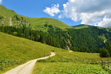 Mountains in High Tauern. Austria and a road across an alpine pasture with Hubertus chapel