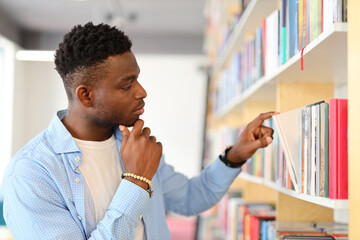 African student standing in front of a bookshelf and pointing at a book