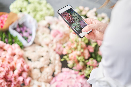 A woman takes a photo on her phone of flowers. Floral shop concept . Florist woman creates flower arrangement in a wicker basket. . Flowers delivery. A woman writes a video blog or online course