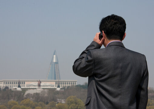 North Korean man calling with his mobile in front of the pyramid-shaped Ryugyong hotel., Pyongan Province, Pyongyang, North Korea