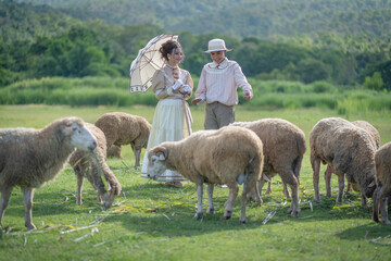 Teenage boy and girl in ancient-style costumes holding an umbrella happy together in the sheep...