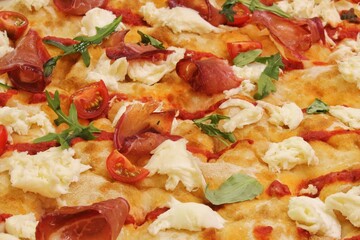Close-up of filling freshly Italian delicious baked pizza Parma with prosciutto, cheese, tomato and herbs. Composition of neapolitan pizza ingredients
