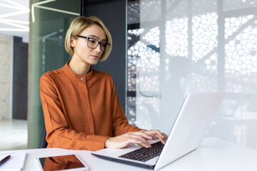Serious and confident woman boss working at workplace inside office with laptop, business woman...