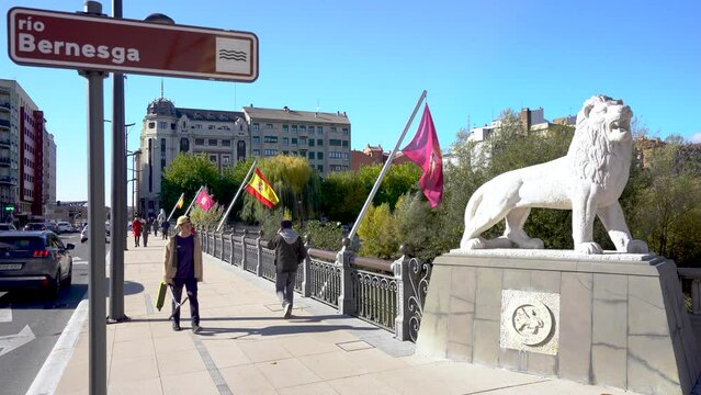 Leon, Spain - November 12 2022:  "PUENTE DE LOS LEONES" Bridge in city center of Leon. Spanish and Leon flag. One of the four statues, representing a lion, positioned one at each corner of the bridge
