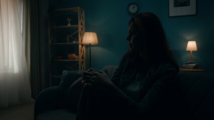 Devastated, detached, lonely young woman sits on a sofa in a dark room close up. Woman desperately thinking about personal problems, going through a crisis. Hopelessness. The concept of mental health.