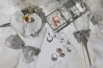 Wedding details in silver color on a white background. Wedding rings and earrings with pearls, glasses on silver stands. Gold wedding rings in a glass box.