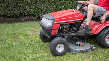 Fototapeta na wymiar Lawn mower mows the grass, a middle-aged male gardener works on a mini tractor