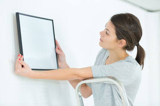woman hanging blank picture frame on wall