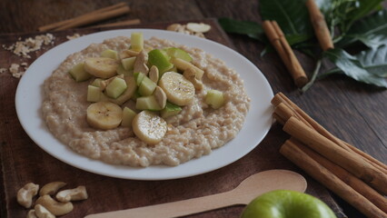 Plate of oatmeal porridge with green apple, cashew and banana. Close up.