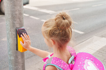 Schoolgirl with schoolbag presses yellow button pedestrian crossing to turn on green light traffic...