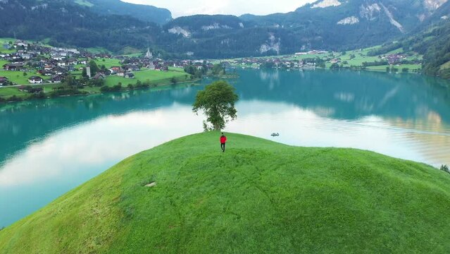 A man in a red coat walks on a hill in front of Lake Brienz 
