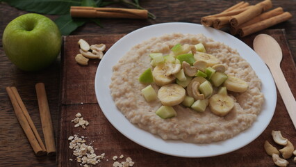 Plate of oatmeal porridge with green apple, cashew and banana. Close up.