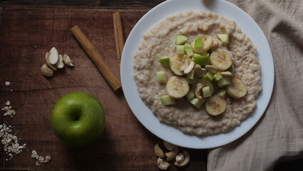 Plate of oatmeal porridge with green apple, cashew and banana. Close up.