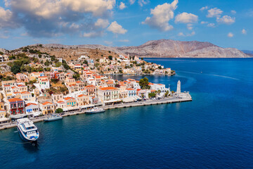 Obraz premium View on Symi (Simi) island harbor port, classical ship yachts, houses on island hills, Aegean Sea bay. Greece islands holidays vacation travel tours from Rhodos island. Symi, Greece, Dodecanese.