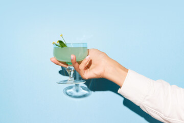Women hand holding glass with margarita cocktail on light blue pop art background. Copy space for...