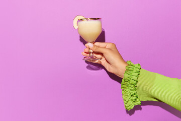 Horizontal photoshoot of female hand holding glass of pina colada on light pink background....
