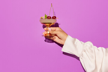 Woman hand holding aperol cocktail decorated cherries on violet background.