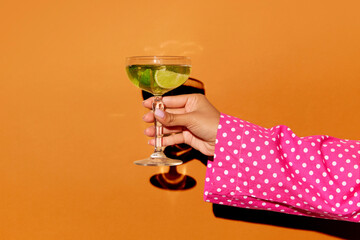 Exclusive alcoholic drink. Female hand holding glass with cocktail mojito with lime over bright...