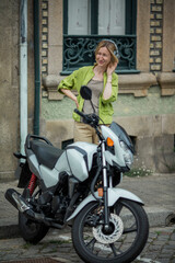 Fototapeta na wymiar A woman wearing headphones standing in the street near a motorcycle.