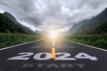 Fotobehang 2024, the new year 2024 or the beginning of the concept of the word 2024, written on a road in the middle of a paved road with a sunset mountain backdrop Planning ideas and challenges © prirach