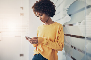 Young businesswoman sending text while leaning against a glass wall