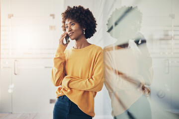 Young businesswoman talking on her phone while leaning against a glass wall