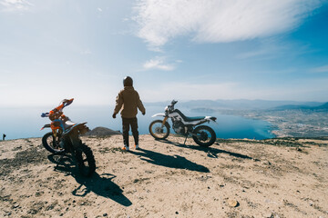 Female rider relaxing in enduro offroad motorcycle travel on mountain top, beautiful sea shore and...