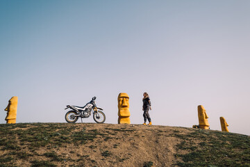 Female traveling on off-road motorcycle near the wooden copies of Moai Statues on sea coast