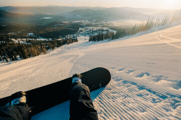 female snowboarder lying on the snow on  steep slope groomed and prepared for skiing, relaxing after riding, enjoying stunning view of winter mountains