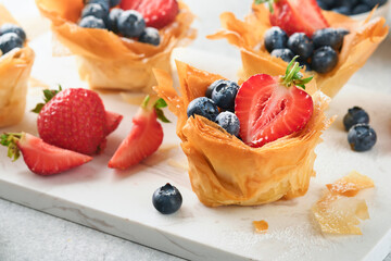 Phyllo or filo pies with fresh berries strawberries and blueberries, cheese filling topped with fresh mint on white plate. Homemade Filo pastry paskets. Delicious filo pastry dessert.