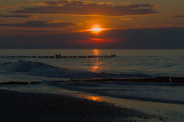 A deep red-orange sunset over the calm Baltic Sea. The sun bathes the sky and the water in a sea of glowing colors. A beautiful sight that radiates peace and tranquility.