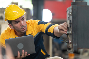 Caucasian male engineer in helmet working in industrial factory. Specialist engineer is using laptop and checking machine