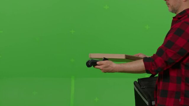 Caucasian male courier passing a box of pizza on green screen chroma key background. Man hold wireless bank payment POS terminal to process acquire credit card payment. Copy space mock up advertising