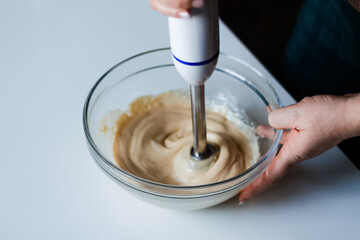 A chef's skilled hands blend homemade mayonnaise with olive oil using a blender. Watch the step-by-step preparation of this creamy sauce in a glass bowl. Out of focus