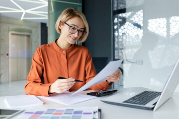 Young successful business woman working inside office with documents, woman satisfied with achievement results reviewing contract, bills and documents, financier in glasses smiling.