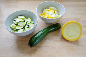 Green and yellow zucchini, whole and chopped in a bowl, ingredient for various vegetable dishes on a wooden kitchen board, vegetarian cooking concept, selected focus