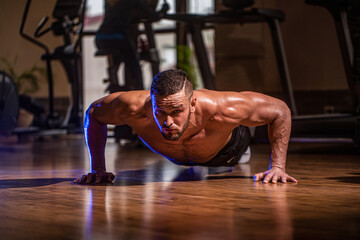 Muscular and strong guy exercising. Muscular male doing push-ups. Slim man doing some push ups a the gym. Man doing push-ups. Muscular man doing push-ups on one hand against gym background. Sport