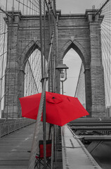Black and white Brooklyn Bridge architectural details with a red umbrella and a red chair.