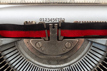 typing with an old typewriter. The numbers from 0 to 9 and the lowercase alphabet, written on a white sheet of paper, with a two-tone, black and red ribbon, and the rest of the steel mechanisms