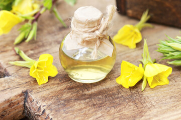 Evening primrose oil in glass bottle with flowers on wooden rustic background, closeup, natural...