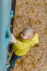 Fototapeta na wymiar Boy At The Climbing Wall Without A Helmet, Danger At The Climbing Wall. Little Boy Climbing A Rock Wall Indoor