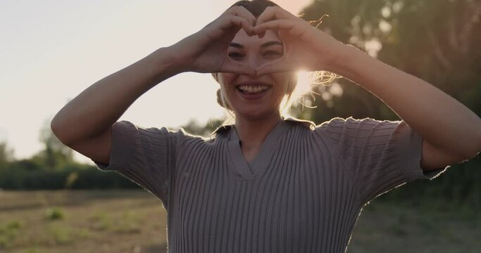 Woman making heart shape with hands during sunset
