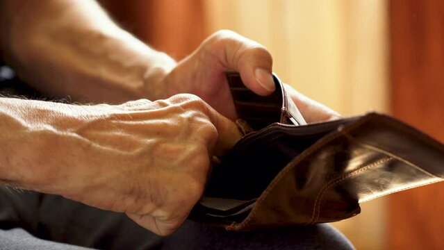 An elderly man's hands, covered with knotted veins, search for coins in his wallet