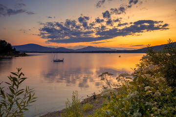 Widok na letni zachód słońca, jezioro z żaglówkami, niebo z chmurami w tle, Polska © anettastar