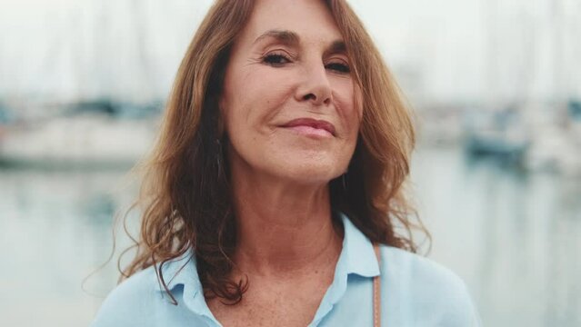 Beautiful middle-aged woman stands in the port raises her head and looks at the camera with smile